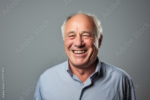 Portrait of a happy senior man laughing and looking at camera against grey background