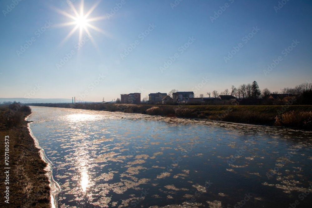 Mures River with pieces of ice floating on the surface flowing through the town of Reghin