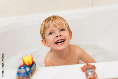 Portrait of a happy little boy in the bath. Smiling child playing with toys while bathing in the bathtub