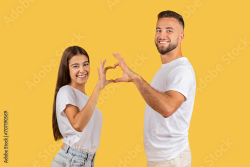 Happy couple in white t-shirts making a heart shape with their hands