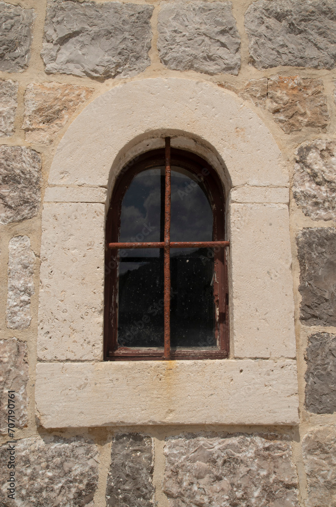 Old arched window  with metal grill on stone facade in Montenegro