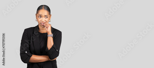 Pensive African American businesswoman biting her nail, looking away with a concerned expression
