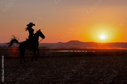 silhouette cowgirl in the sunset riding in the prairie near a waterhole © poco_bw