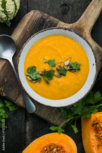 Pumpkin soup and organic pumpkins on wooden table. Seasonal autumn food - Spicy pumpkin soup in bowl.