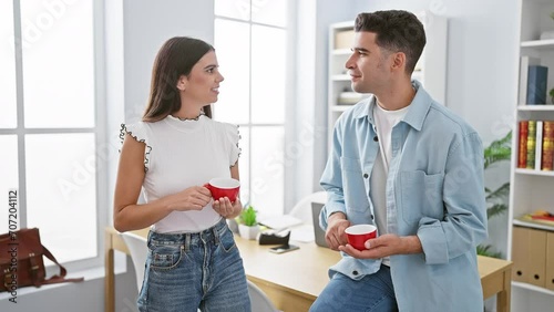 A man and woman, both employees, engage in a conversation with coffee cups in a modern office environment. photo