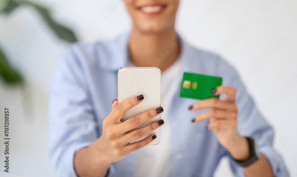 Blurred young woman smiling while holding a smartphone and credit card Blurred young woman smiling while holding a smartphone and credit card