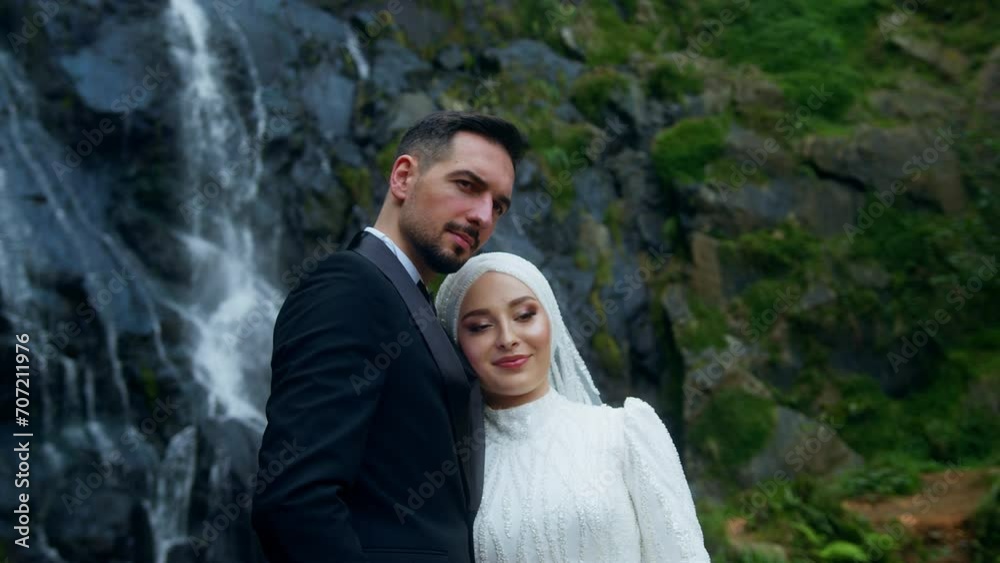 Young happy bride and groom standing in front of a waterfall smiling and posing outdoors