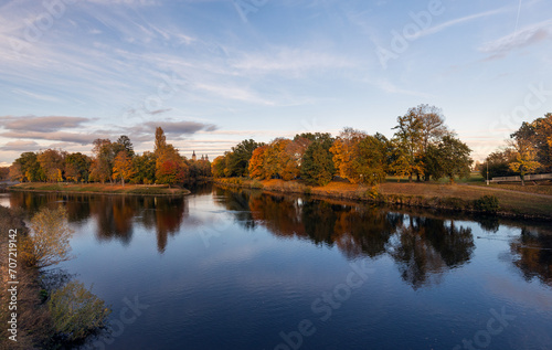 Autumn landscape with river and trees in the park at sunset.