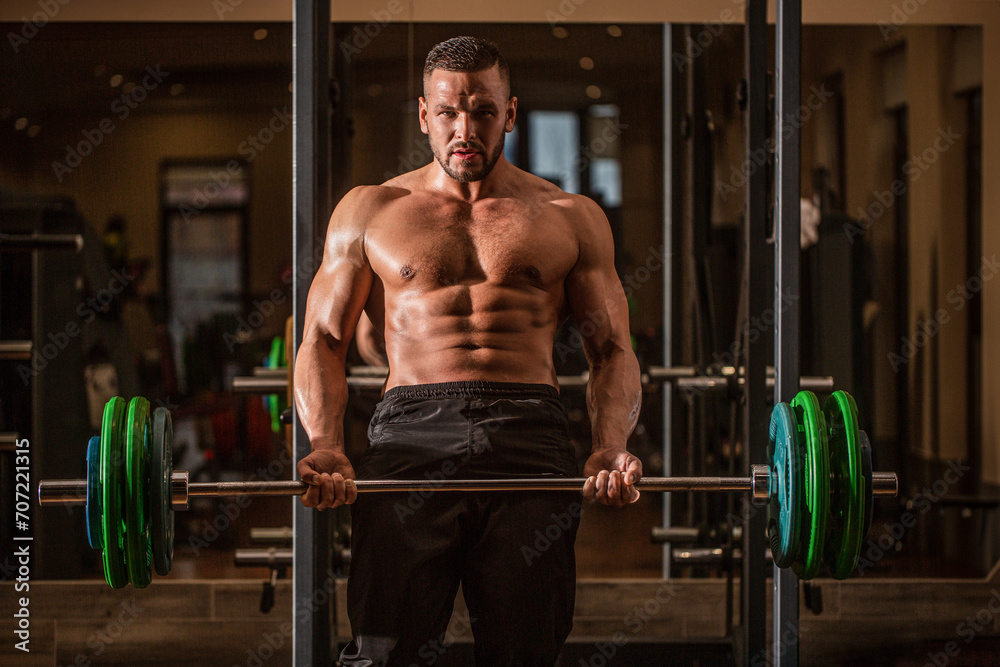Barbells workout. Bodybuilder athletic man with six pack, perfect abs, shoulders, biceps, triceps, chest. Athletic guy standing with barbell, workout in gym. Muscular man workout with barbell at gym Barbells workout. Bodybuilder athletic man with six pack, perfect abs, shoulders, biceps, triceps, chest. Athletic guy standing with barbell, workout in gym. Muscular man workout with barbell at gym