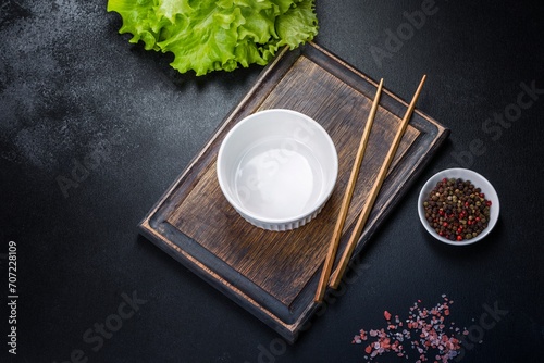 An empty white bowl and sticks on a wooden cutting board