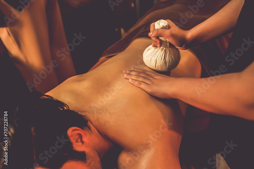Fotografia Hot herbal ball spa massage body treatment, masseur gently compresses herb bag on man body