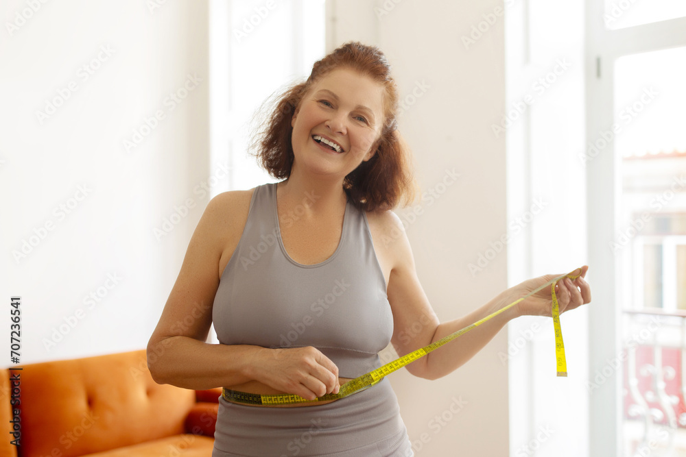 Happy senior woman measuring her waist with tape, showing her fitness progress Happy senior woman measuring her waist with tape, showing her fitness progress
