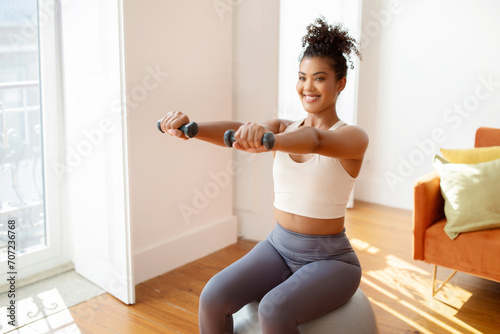 Fit woman sitting on balance ball lifting weights exercising indoor
