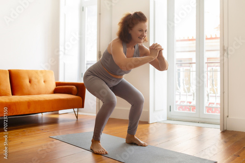 Smiling senior woman making squat exercise at home photo