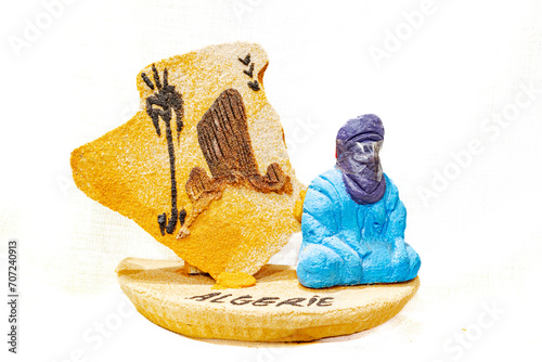 Sand sculpture of Algerian geographic map and painting of sahara desert rocky mountain, palm tree and three birds. A tuareg man sitting on the floor cross-legged with french inscription says 