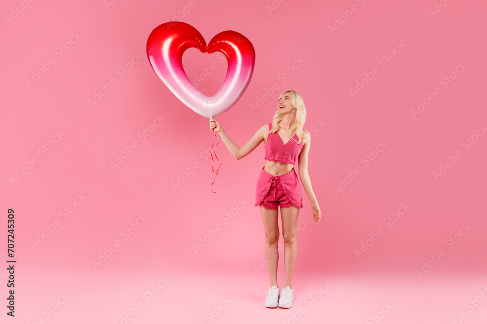 Blonde in pink looking up at heart balloon Blonde in pink looking up at heart balloon