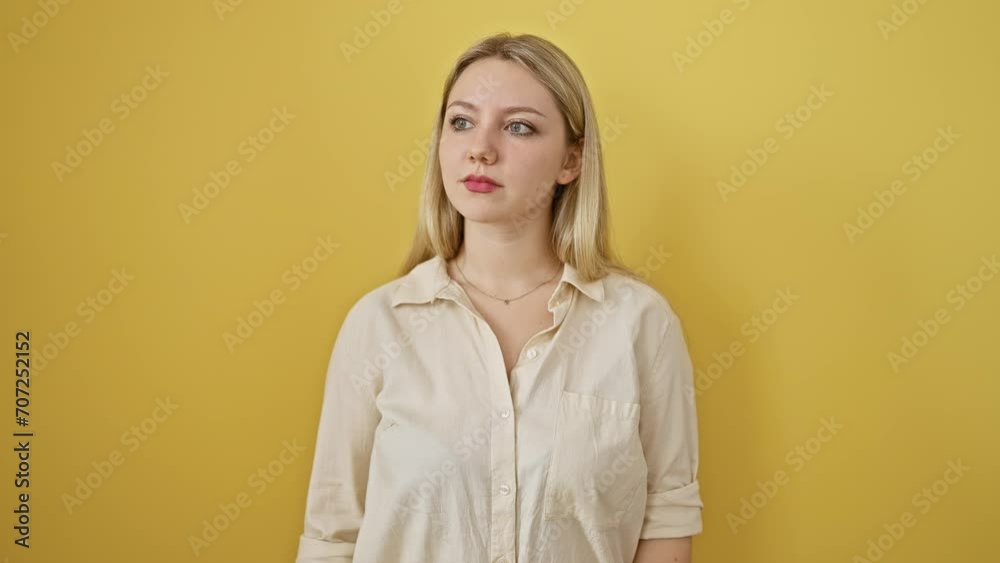 Confident young blonde woman wears simple style, trusts her natural look, standing against an isolated yellow background with serious gaze into camera, earnest expression on her face Confident young blonde woman wears simple style, trusts her natural look, standing against an isolated yellow background with serious gaze into camera, earnest expression on her face
