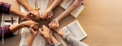 Cropped image of group of people praying together while holding hand on holy bible book at wooden church. Concept of hope, religion, faith, christianity and god blessing. Top view. Burgeoning.