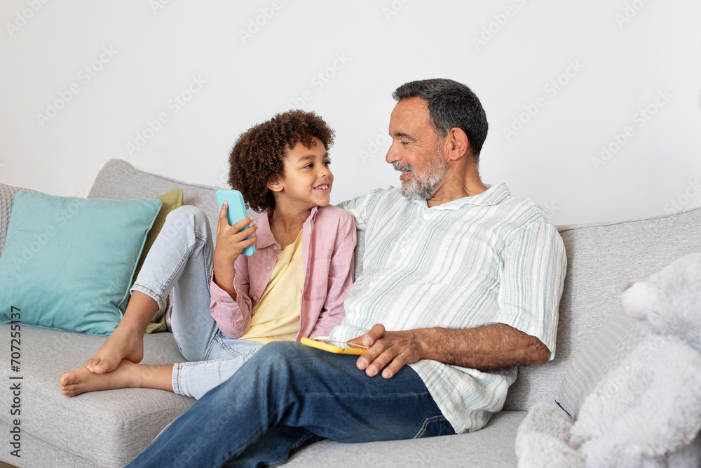 Latin grandpa and grandchild happily using smartphone application at home