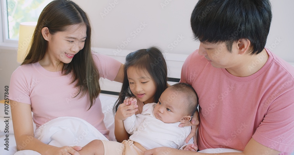 Happy Asian family father mother daughter baby embrace smiling together lying relaxing on white bed in bedroom at home, happy parent and child girl enjoy hugging having fun playing in bedroom