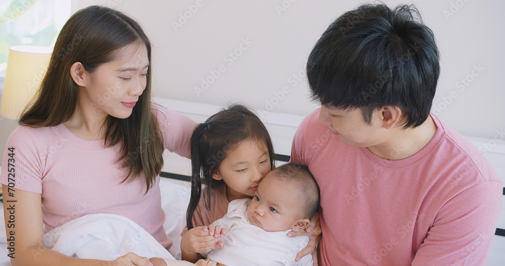 Happy Asian family father mother daughter baby embrace smiling together lying relaxing on white bed in bedroom at home, happy parent and child girl enjoy hugging having fun playing in bedroom