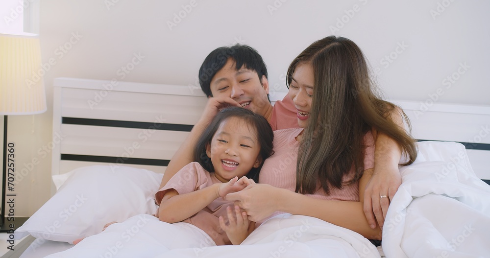 Happy Asian family father mother and daughter embrace smiling together lying relaxing on white bed in bedroom at home, happy parent and child girl enjoy hugging having fun playing in bedroom Happy Asian family father mother and daughter embrace smiling together lying relaxing on white bed in bedroom at home, happy parent and child girl enjoy hugging having fun playing in bedroom