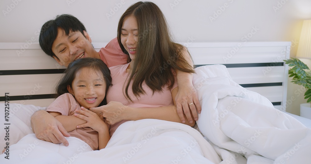 Happy Asian family father mother and daughter embrace smiling together lying relaxing on white bed in bedroom at home, happy parent and child girl enjoy hugging having fun playing in bedroom Happy Asian family father mother and daughter embrace smiling together lying relaxing on white bed in bedroom at home, happy parent and child girl enjoy hugging having fun playing in bedroom