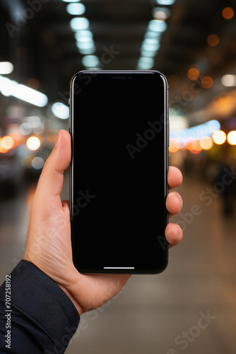 Male hand holding a smartphone with a blank screen on the background of the city