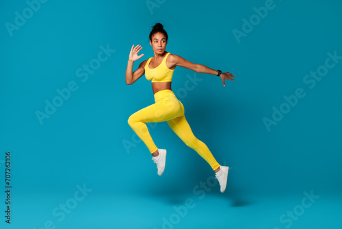 Determined African American fitness woman jumps against blue studio background