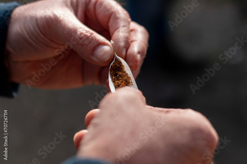Man's hands rolling a cigarette, the paper on the tobacco