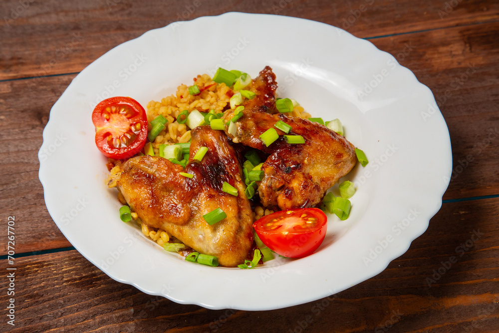Chicken wings baked with bulgur, topped with green onions, garnished with cherry tomatoes on a white plate