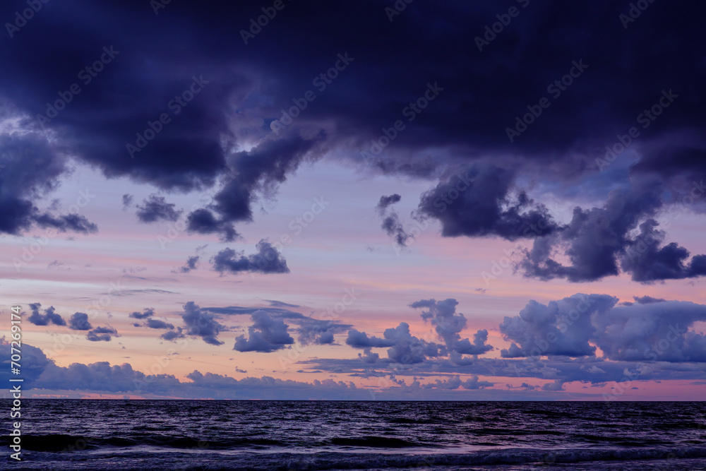 Obraz premium Twilight seascape with layered clouds, radiant sunset hues casting over the undulating ocean waves