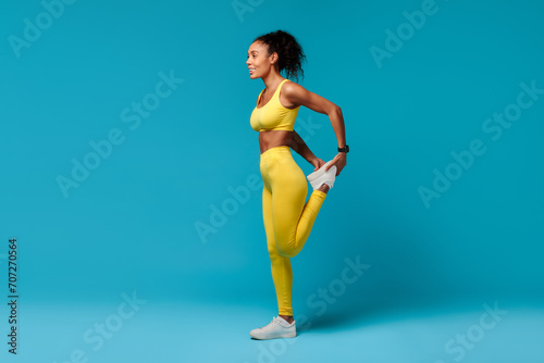 Black woman warming up stretching leg muscles over blue background