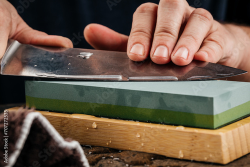 A man sharpens a knife with a grindstone on a rustic wooden table.