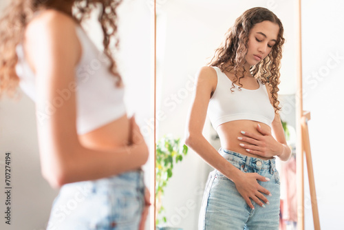 Teenager Girl Touching Stomach Standing Near Mirror At Home photo