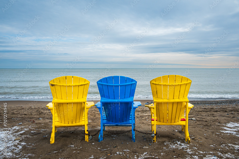 possiblities: three empty colorful beach chairs seen from behind looking out over lake ontario in winter with blue clouds kew beach toronto room for text possiblities: three empty colorful beach chairs seen from behind looking out over lake ontario in winter with blue clouds kew beach toronto room for text
