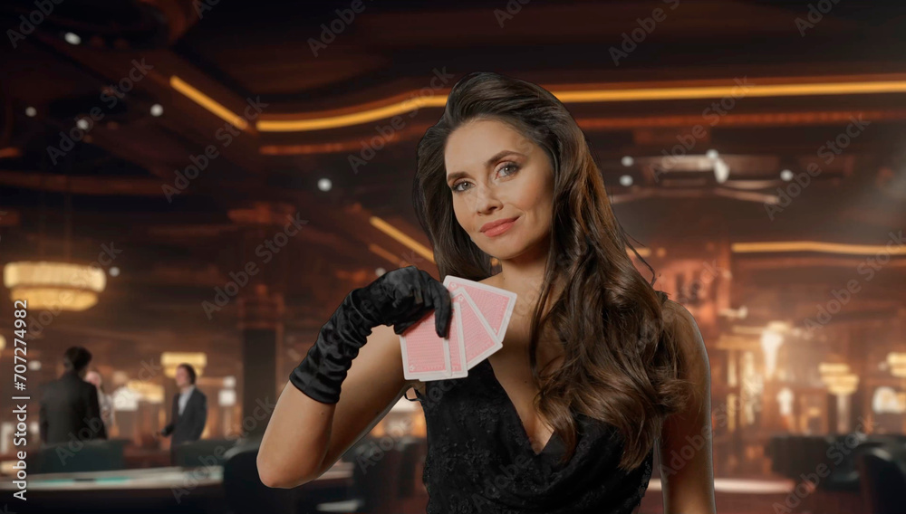 Chic woman in black dress at poker table for blackjack game in casino. Woman holding poker cards, looking at camera and smiling. The concept of casino and gambling.