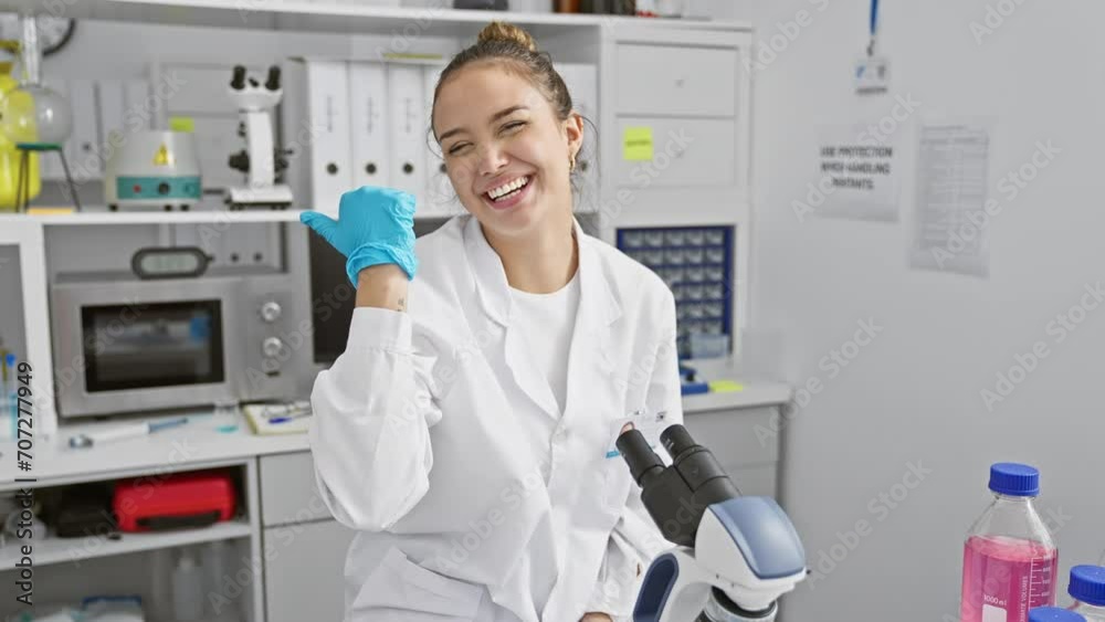 Cheerful young hispanic woman scientist in uniform, giving a thumbs up with an open mouth smile at the lab Cheerful young hispanic woman scientist in uniform, giving a thumbs up with an open mouth smile at the lab