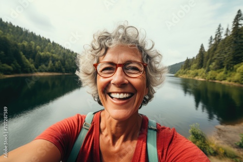 Smiling middle aged woman taking selfie lakeside © NikoG