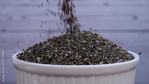 Chia seeds falling into a white bowl in slow motion. Chia seeds are rich in minerals, omega 3 fat, antioxidants and fiber. Healthy food concept.