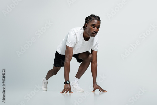 Focused black man in athletic wear poised in starting position for sprint