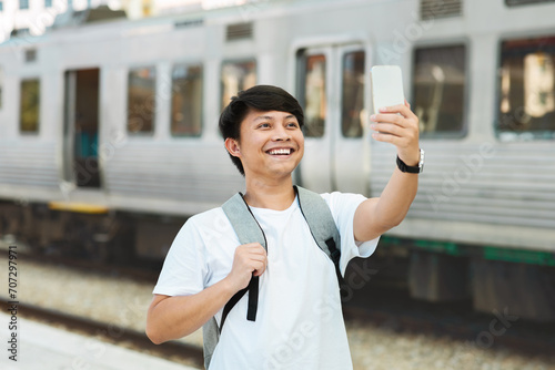 Happy millennial taiwanese guy traveler taking selfie at train station
