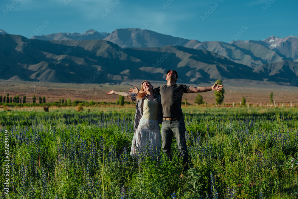 Happy young couple enjoying good weather in a field on mountains background