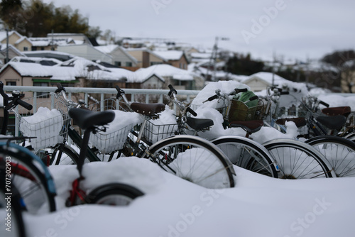 Bicycles covered in snow with blurred residential area in the background.