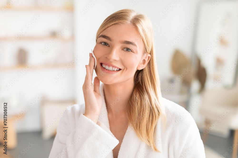 Blonde Woman Doing Facial Skincare With Cotton Pad In Bathroom