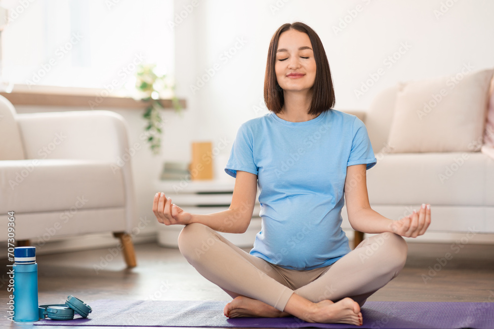 Expectant mother practicing yoga sitting on yoga mat meditating indoor Expectant mother practicing yoga sitting on yoga mat meditating indoor