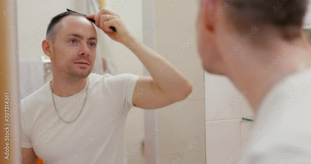 A man combing his hair with a comb while looking in the mirror in the bathroom A man combing his hair with a comb while looking in the mirror in the bathroom