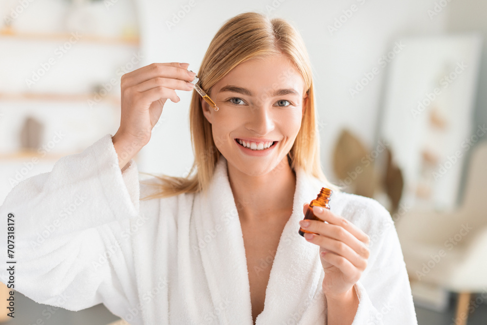 Blonde lady applies facial serum using dropper in bathroom Blonde lady applies facial serum using dropper in bathroom