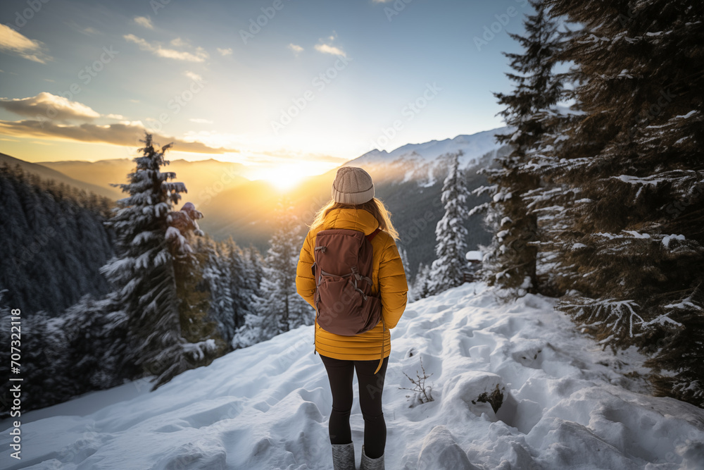 Generative AI back view image of an unrecognizable woman in a yellow jacket standing and observing a sunset in a snowy mountain landscape