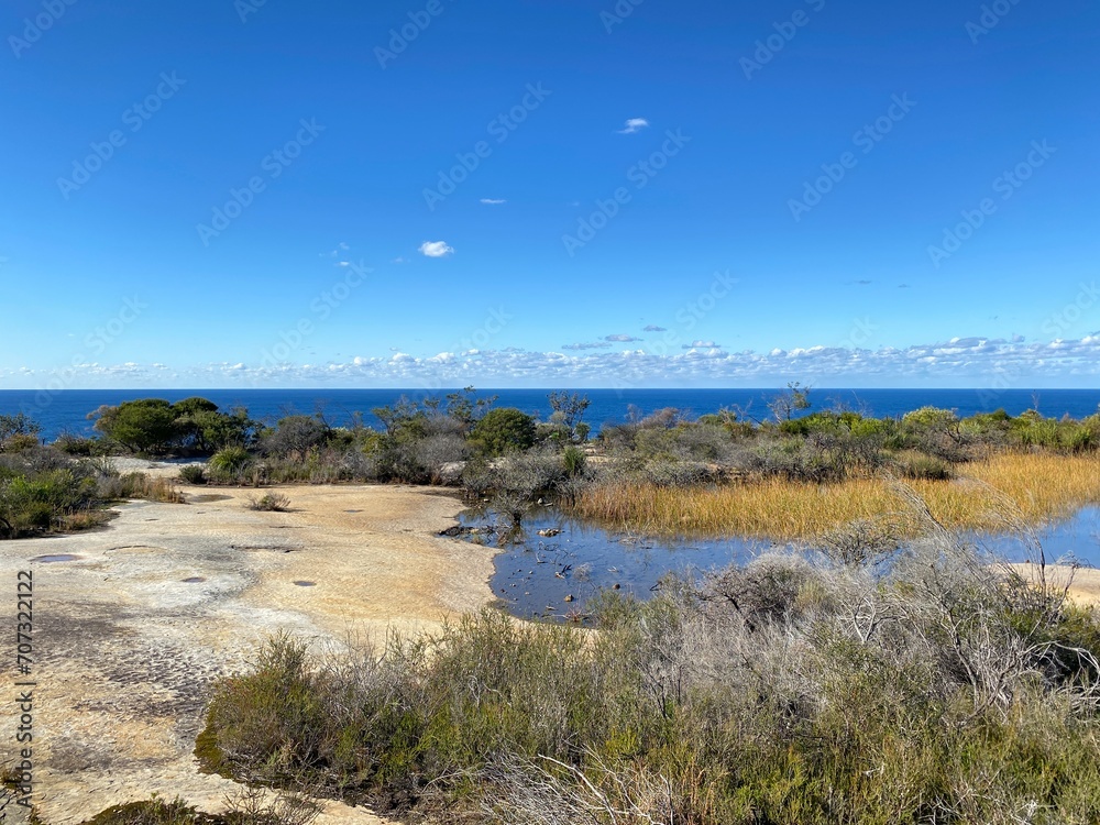 Dry vegetation and rock formation at the summit. Desert rocky plateau. Views from a mountain-top lookout. Australia, Sydney. Ocean at the horizon.